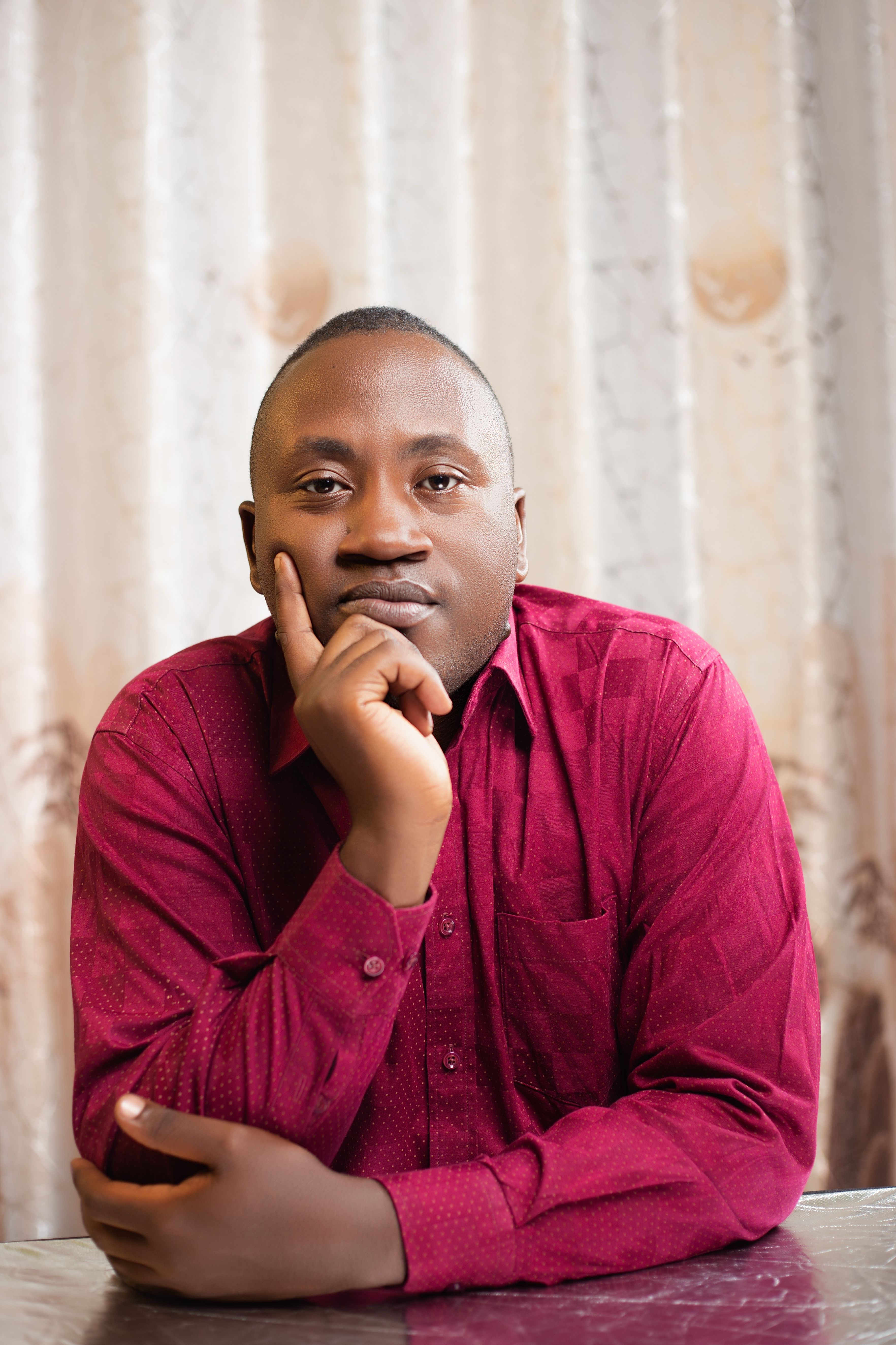 A thoughtful man in a red shirt poses indoors with a contemplative expression.