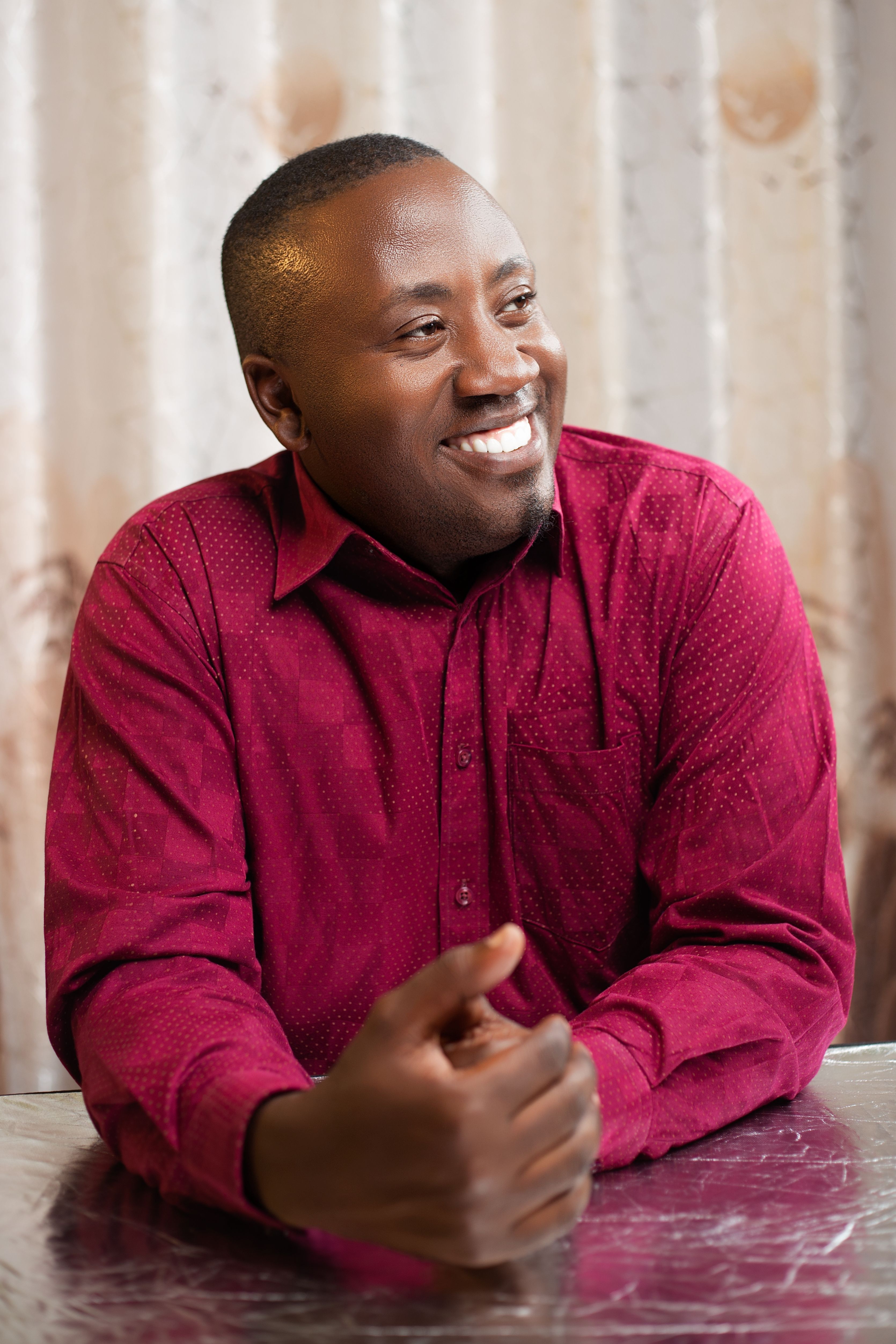 Portrait of a smiling man in a red shirt sitting indoors with a relaxed pose.