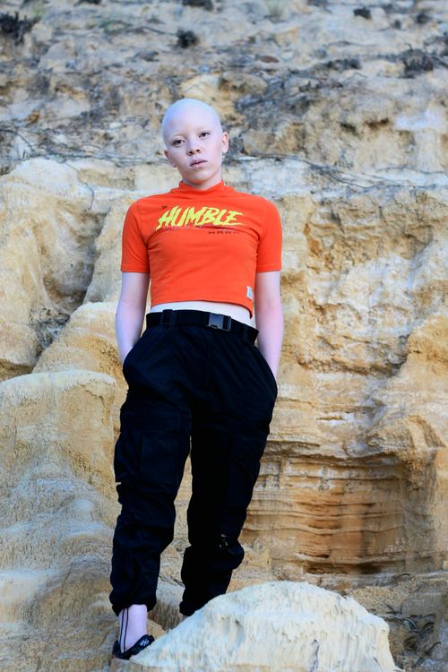 Free A stylish young person stands confidently against a rugged rock wall wearing a 'Humble' shirt. Stock Photo