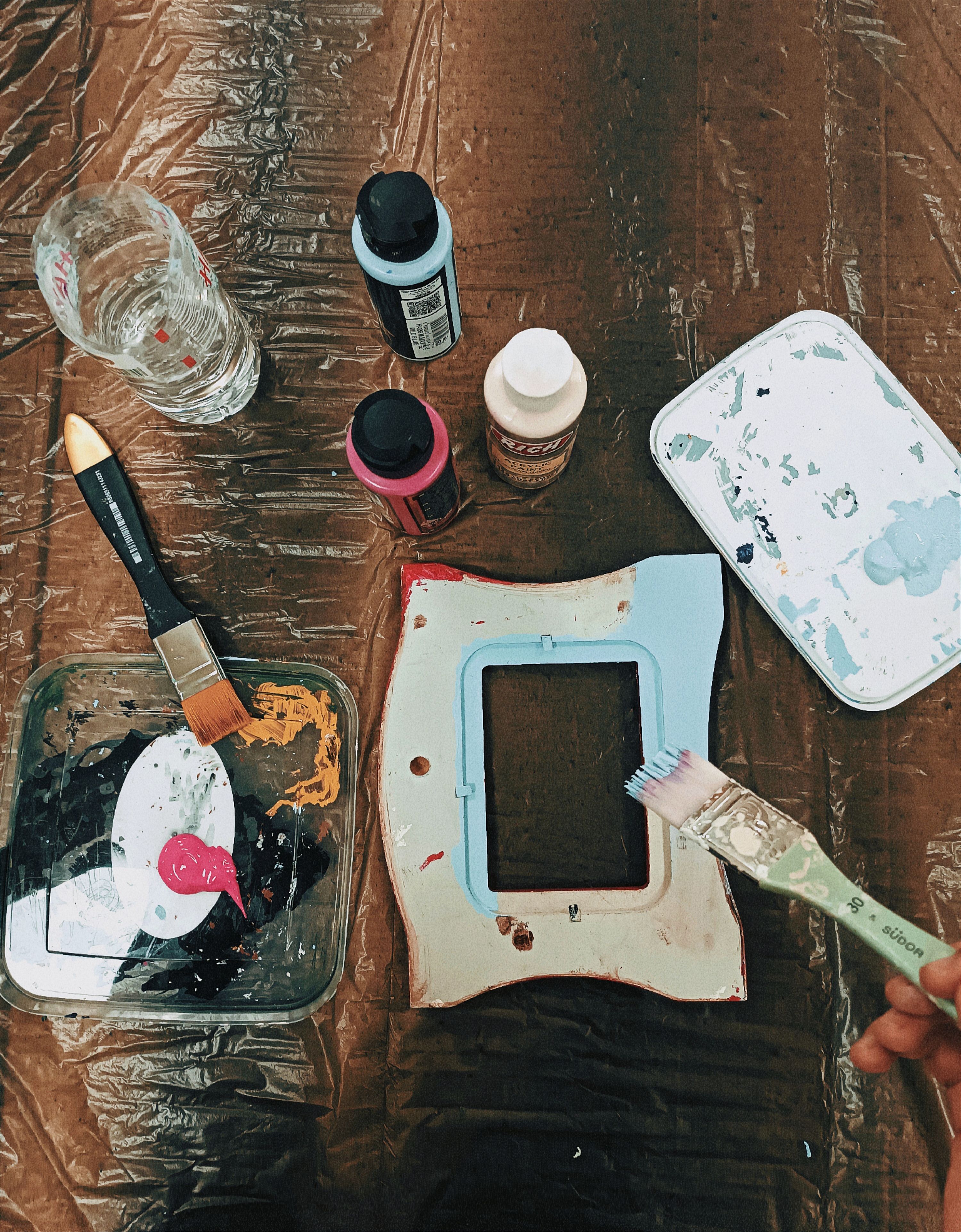 Overhead view of a table with paint supplies and a frame in a home crafting session.