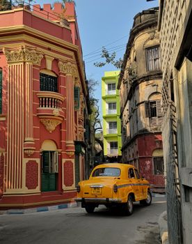 A vibrant scene of a vintage yellow taxi navigating a colorful street in Kolkata, India.