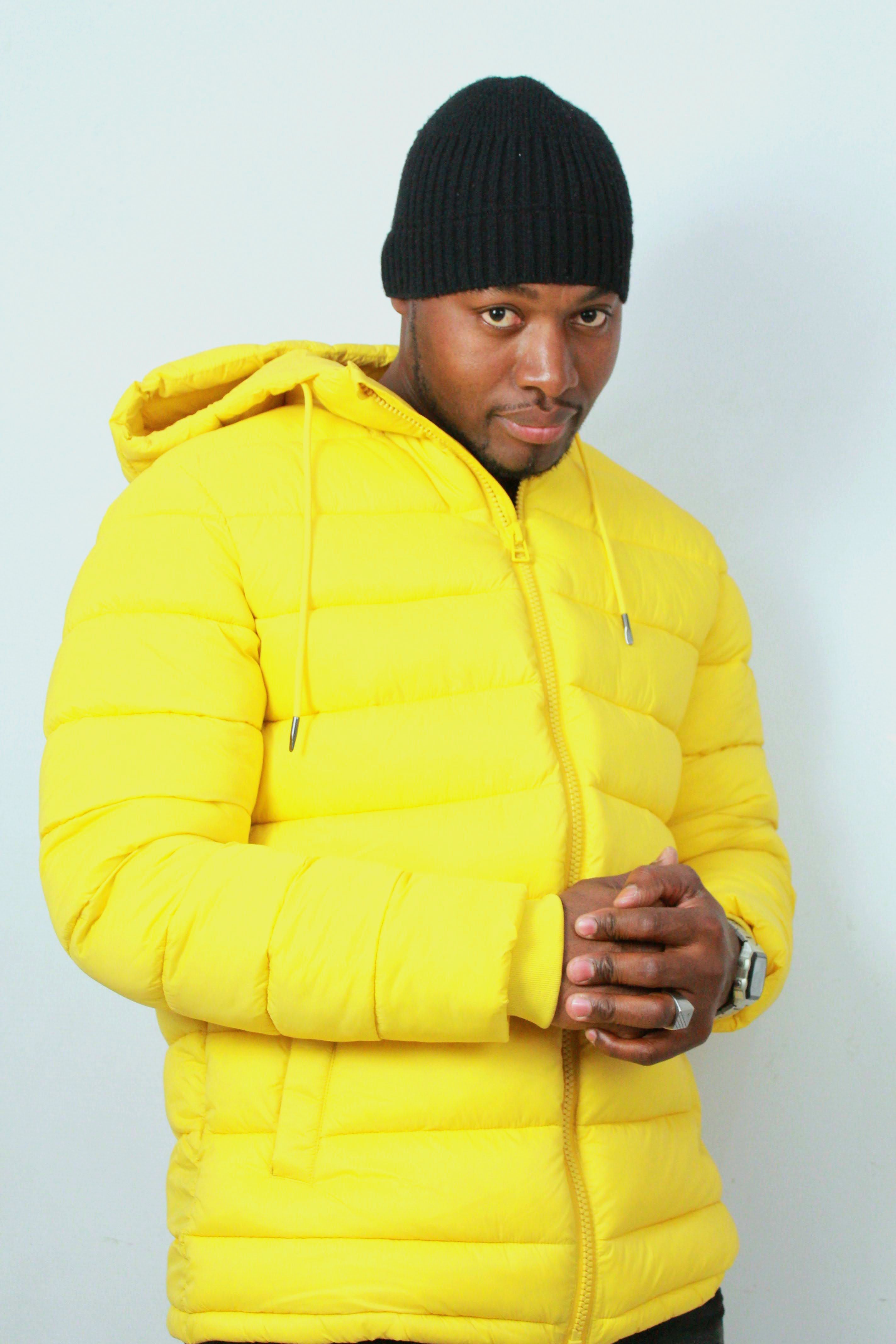 Portrait of a stylish man in a vibrant yellow jacket and black beanie posing confidently indoors.