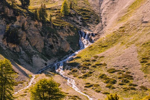 Beautiful waterfall cascading down a rocky hillside in Ceillac, France, surrounded by lush alpine vegetation.