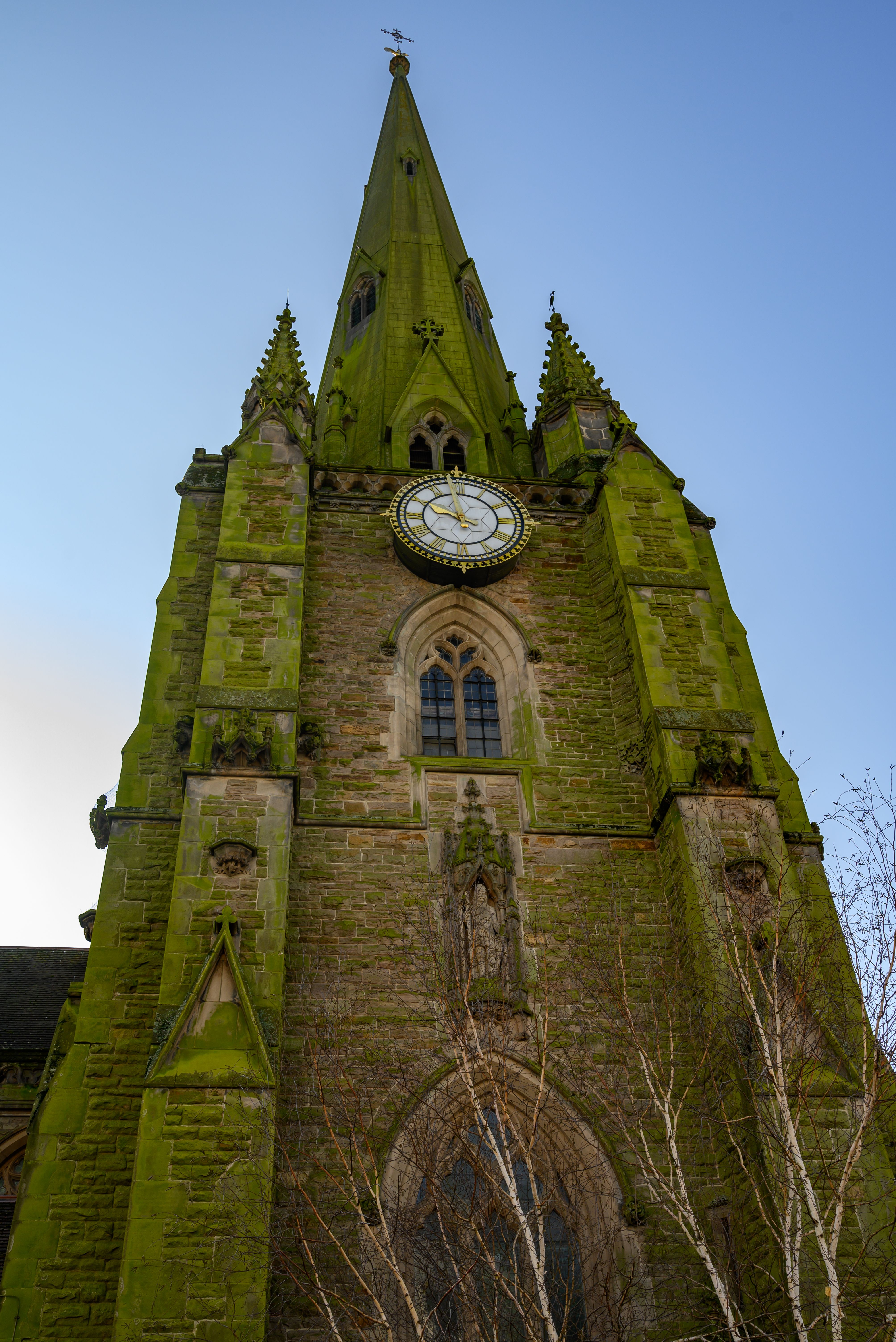Photograph of a towering Gothic-style church with a prominent clock face in England.