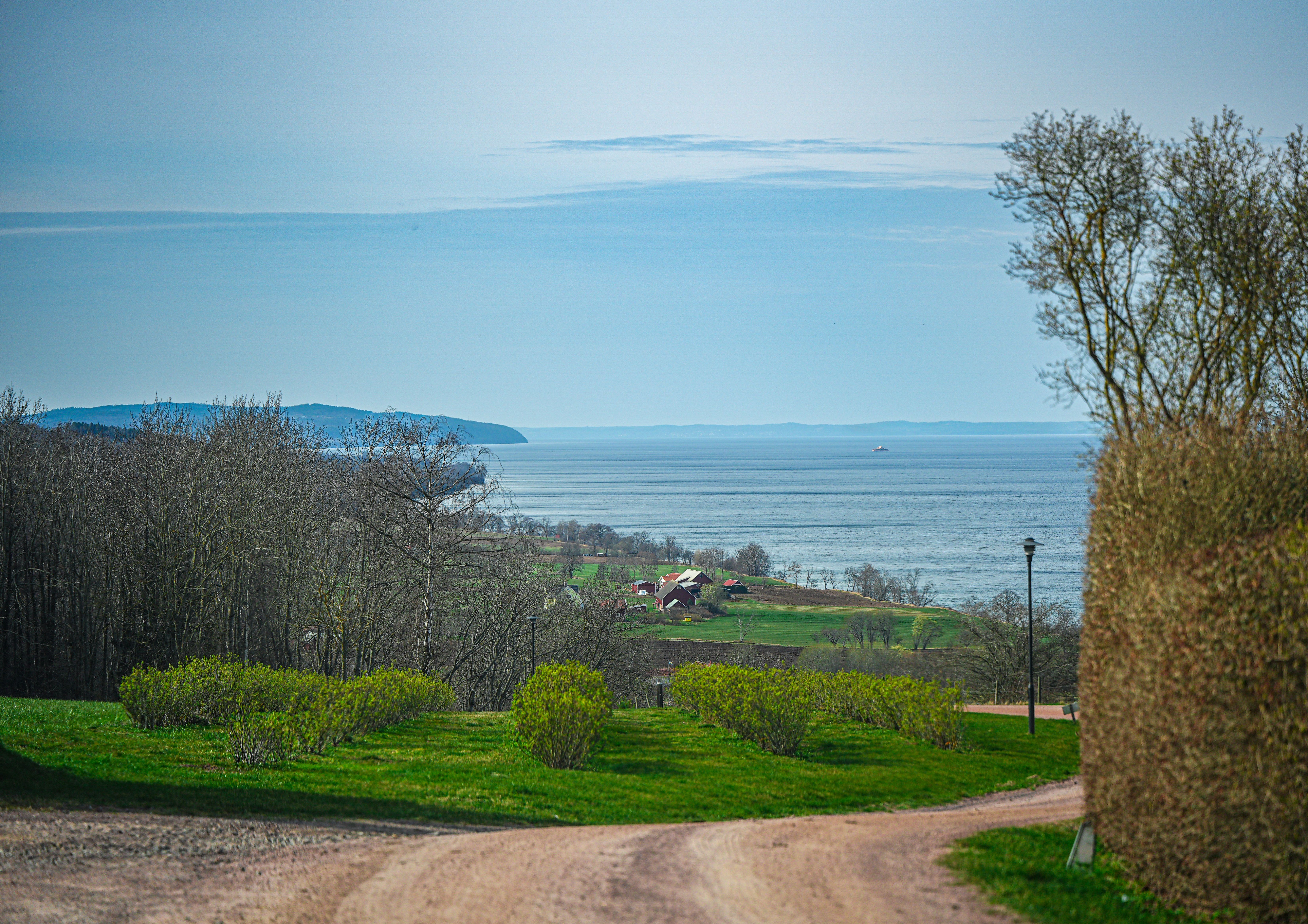 grátis Paisagem rural tranquila com vista desimpedida para o oceano, campos verdejantes e colinas distantes sob um céu azul vibrante. Foto profissional