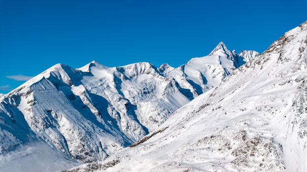 Breathtaking view of snow-capped mountains in Korutany, Austria against a clear blue sky.