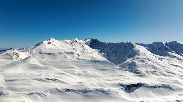 Stunning aerial view of snow-covered mountains under a clear blue sky in Korutany, Austria.