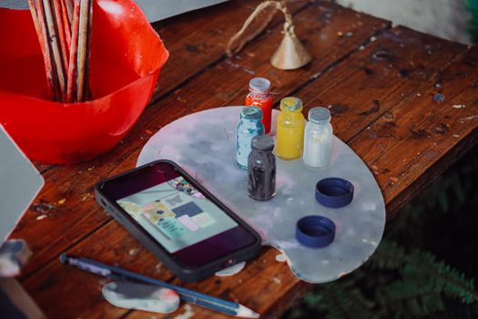 A vibrant artist's workspace with paint bottles, smartphone, and palette on a wooden table in Addis Ababa.