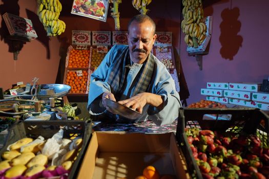 Man weighing produce at a colorful fruit market stall with a variety of fresh fruits.