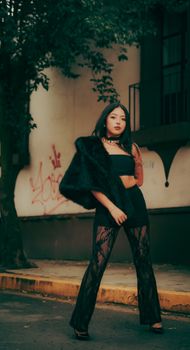 Chic woman in lace pants and fur wrap poses confidently in a moody urban backdrop.