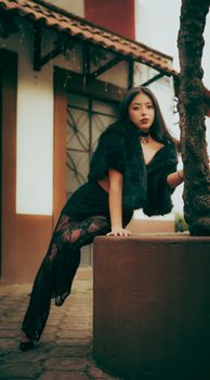 A fashionable woman poses elegantly outdoors against an urban backdrop, exuding sophistication.