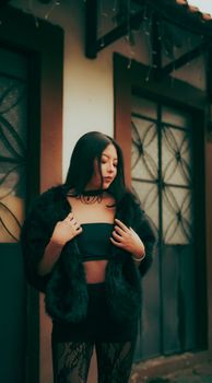 Stylish woman in black attire, posing outdoors against urban backdrop. Chic and modern.
