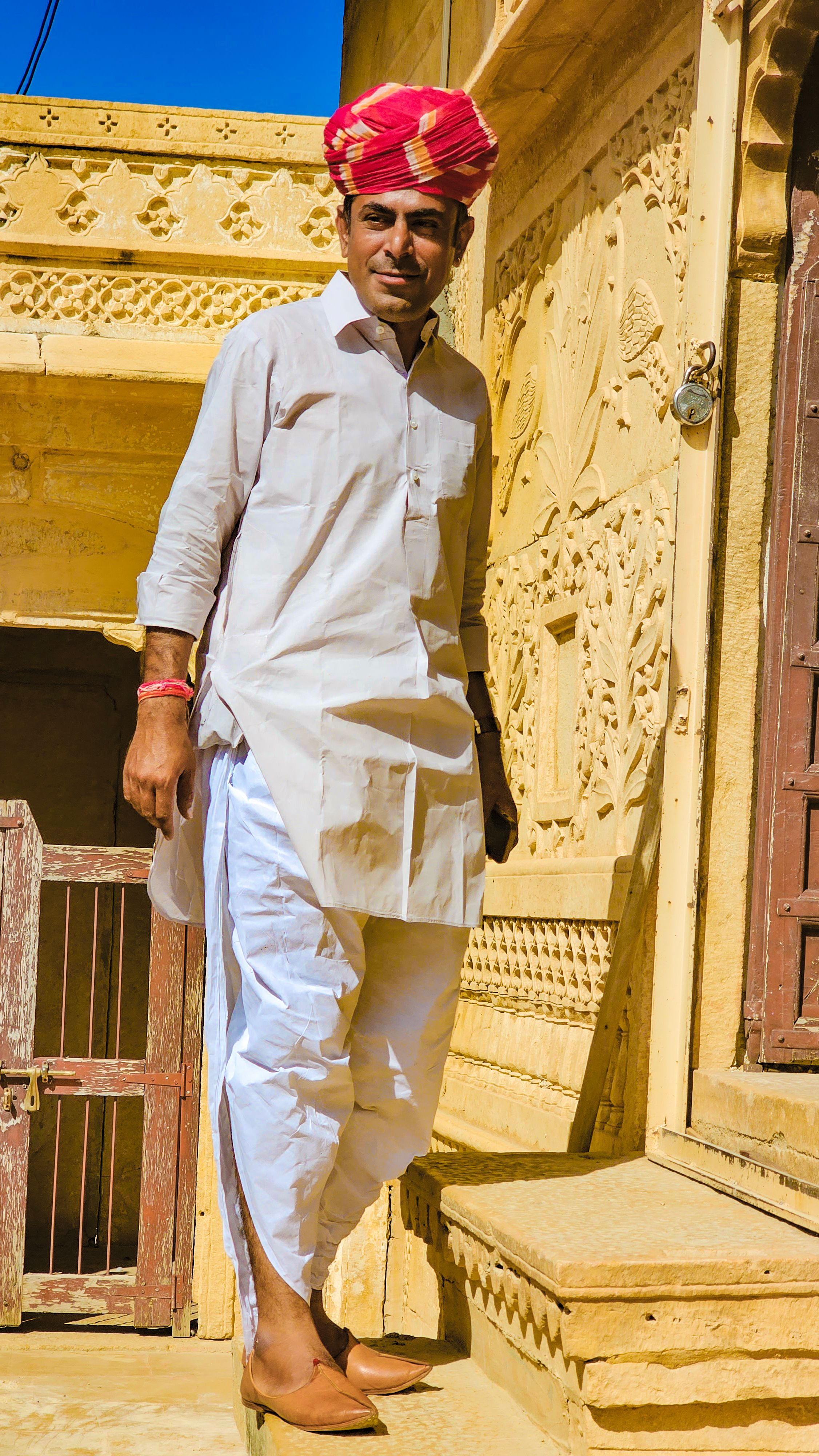 A man in traditional Rajasthani attire stands outside a historic building.