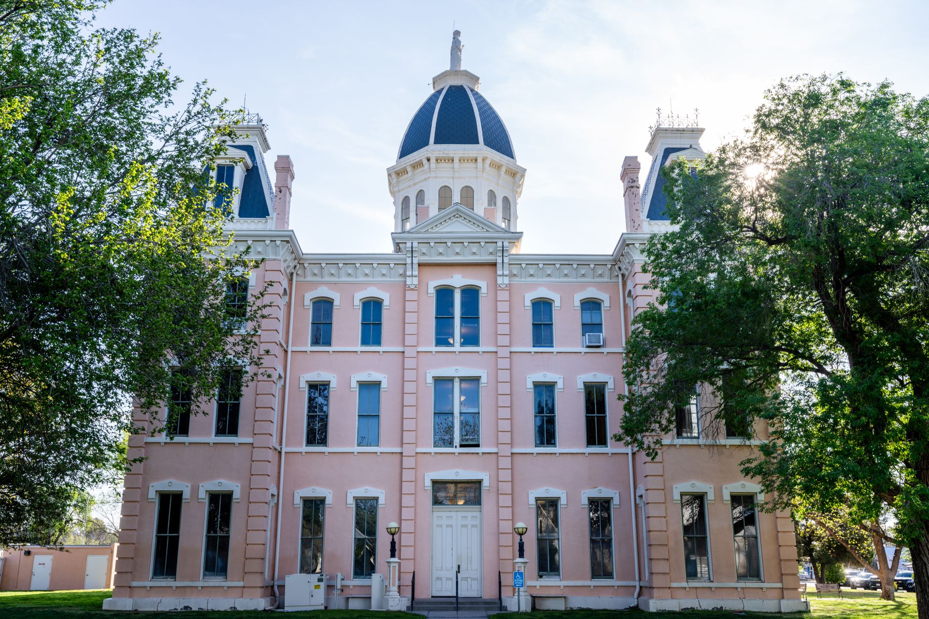 Front view of the iconic Presidio County Courthouse in Marfa, Texas, framed by trees under a clear sky.