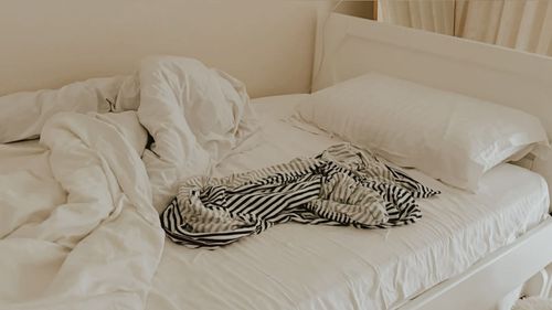 Free An unmade bed with crumpled linens and a striped shirt adding a cozy feel. Stock Photo