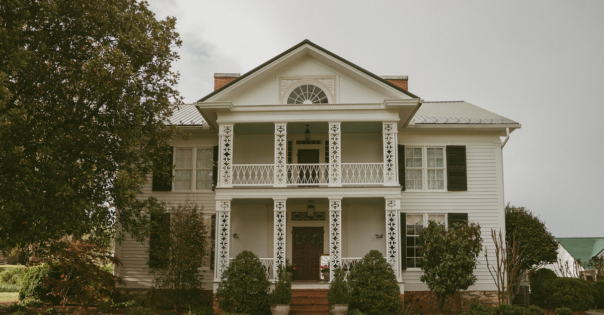 A traditional white colonial-style house with ornate porch and lush greenery.