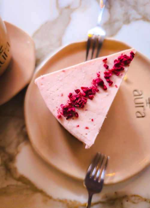 Free Close-up of a raspberry-topped cheesecake slice on a stylish plate in a warm cafe setting. Stock Photo