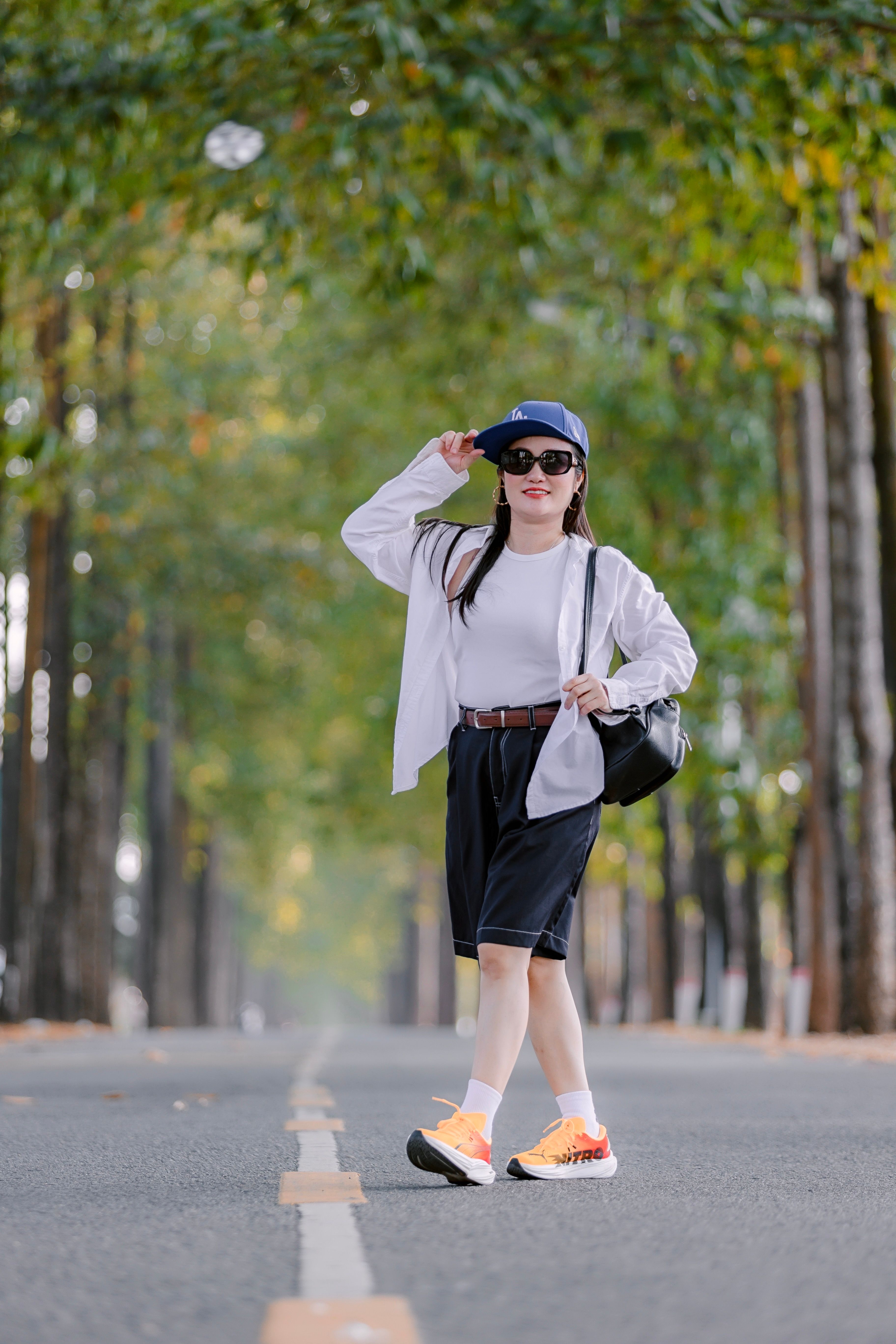 A fashionable woman poses confidently on a picturesque, tree-lined street, exuding modern urban style.