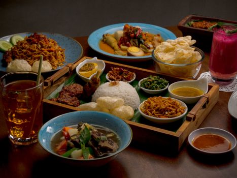 A diverse spread of traditional Indonesian dishes displayed on a wooden table indoors.
