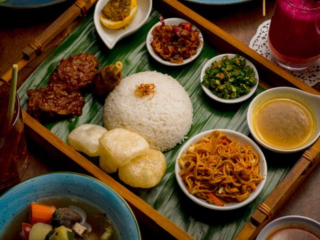 A vibrant display of Nasi Campur featuring rice, satay, noodles, and sides, presented on traditional banana leaf.