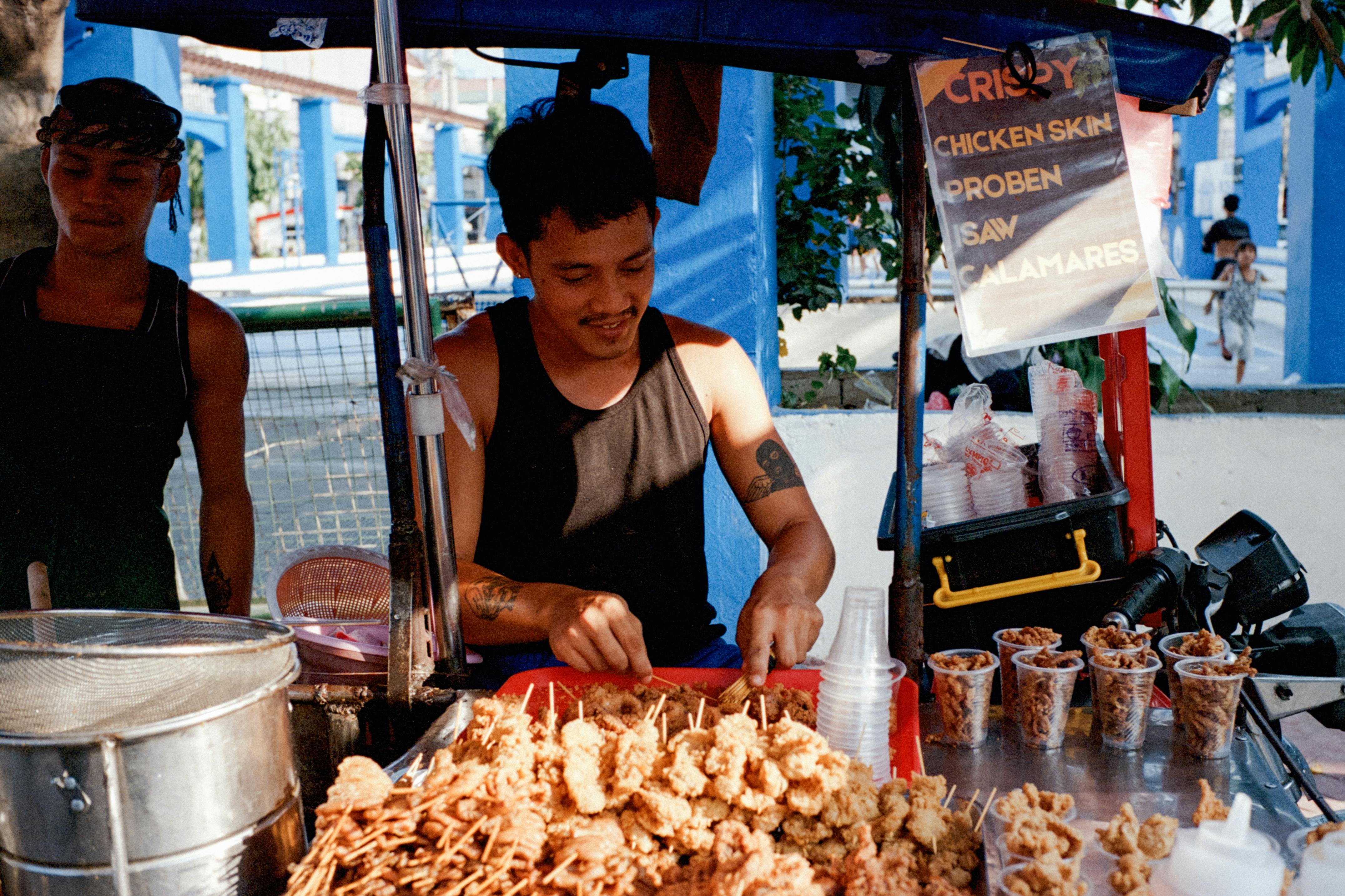 A street vendor serves skewers and crispy snacks at a vibrant food stall in Manila, Philippines.