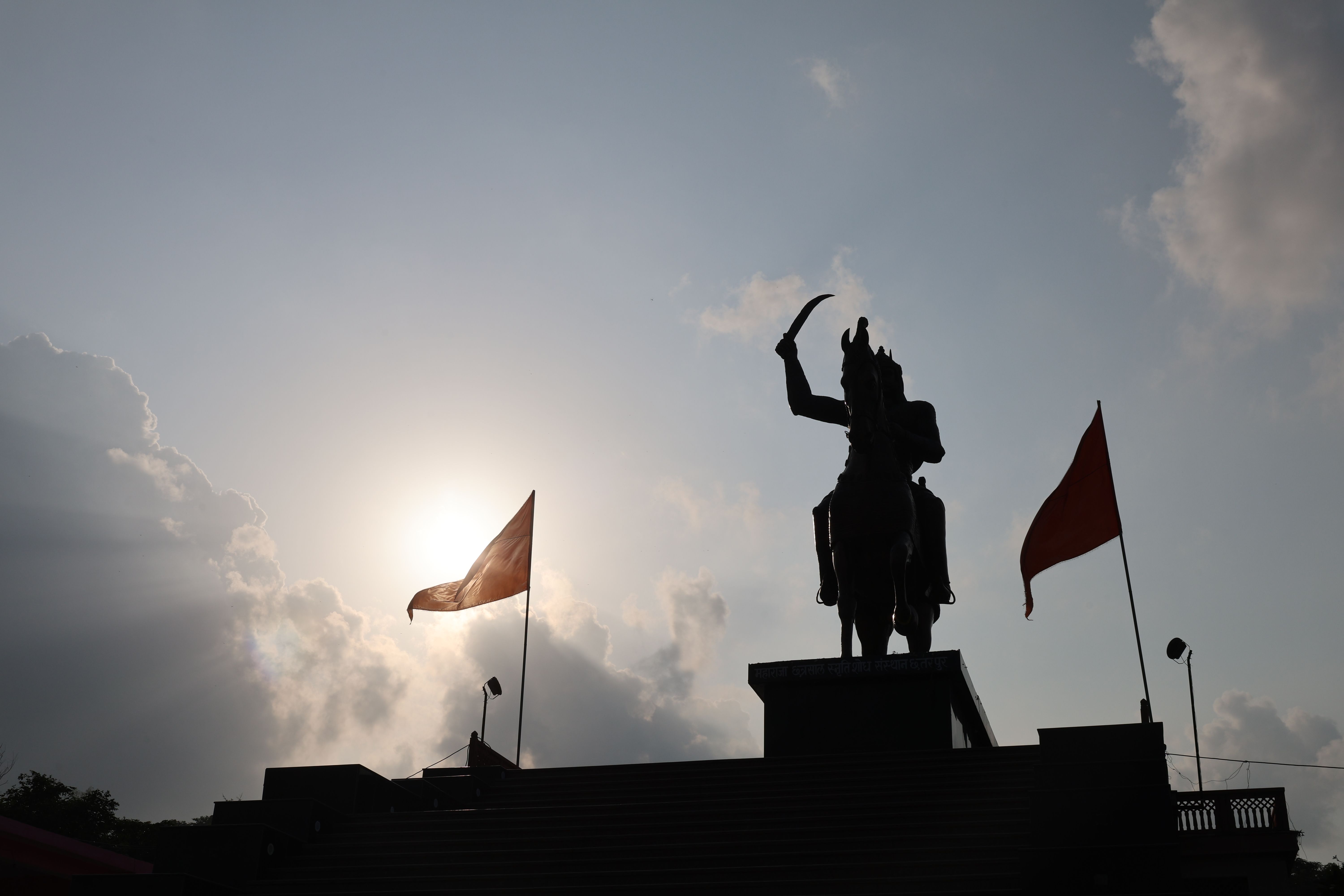 Silhouette of an equestrian statue with dramatic sky and flags at sunset.