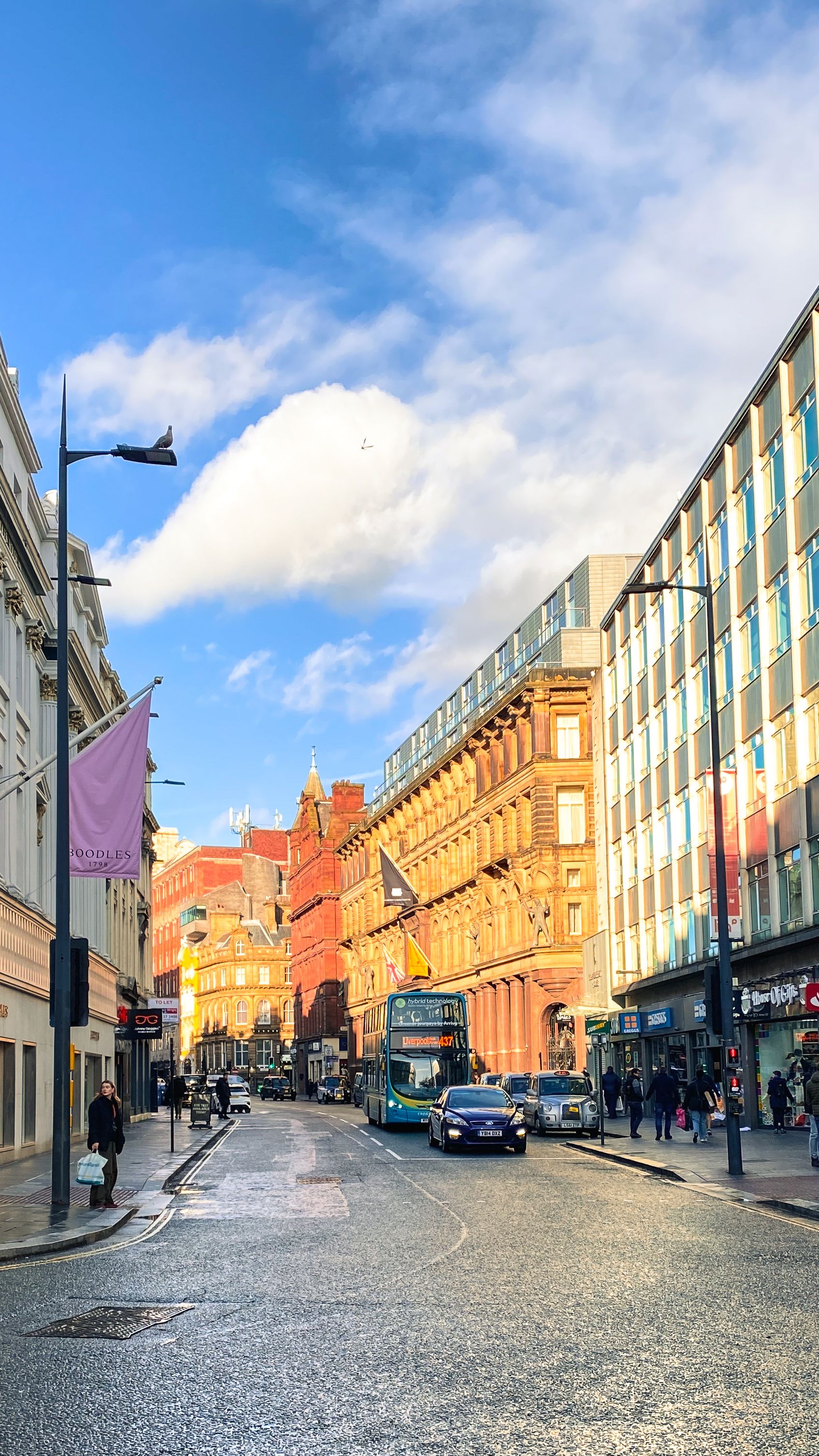 Vibrant Liverpool street scene featuring classic red brick architecture, busy traffic, and bright blue sky.