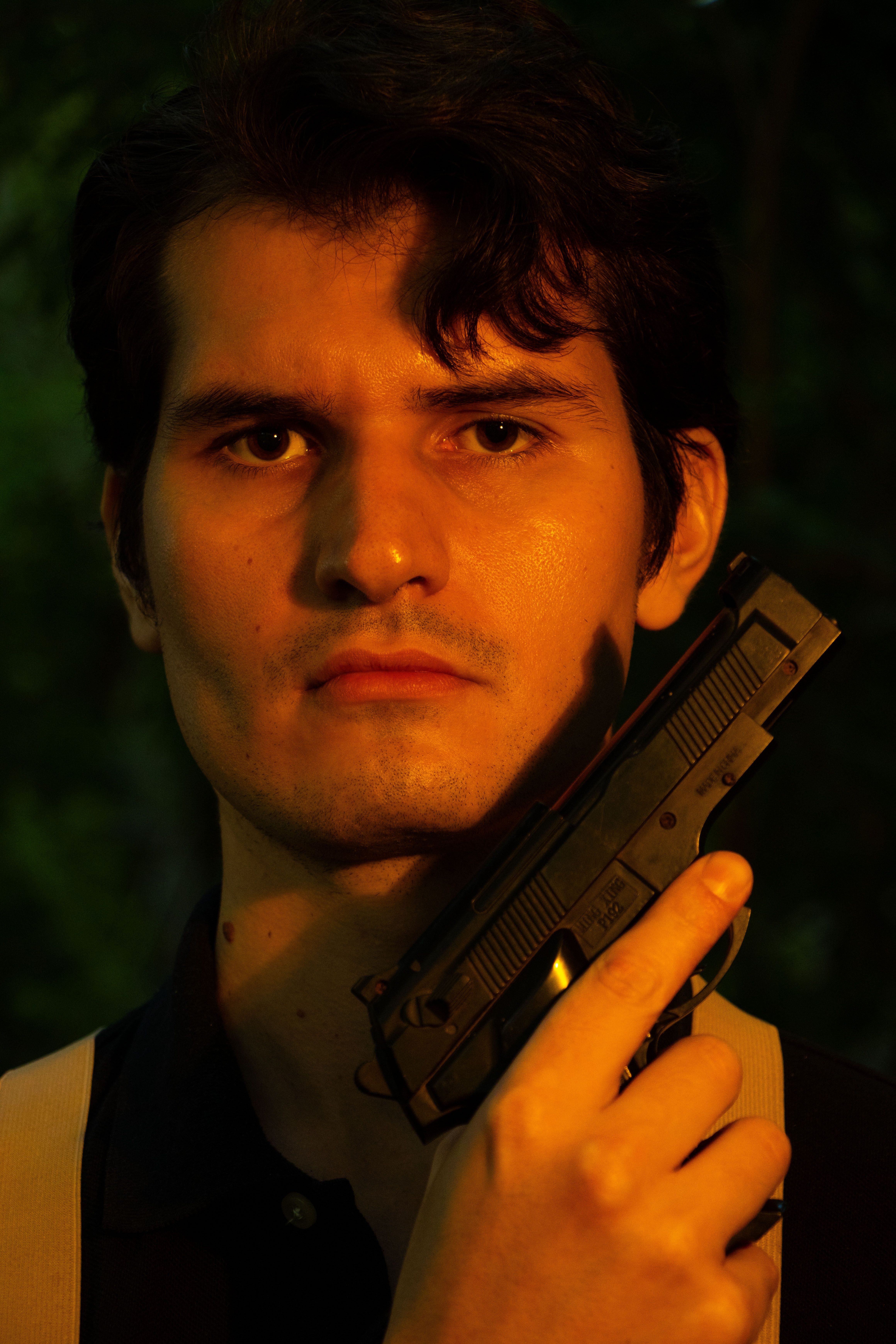 A young man with a serious expression holding a handgun outdoors in Lima, Perú.