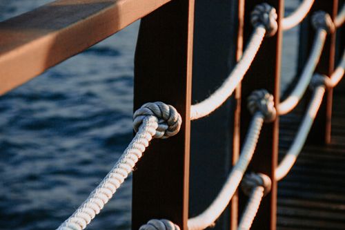 Free Detailed view of a nautical rope on a wooden dock with serene water in the background. Stock Photo