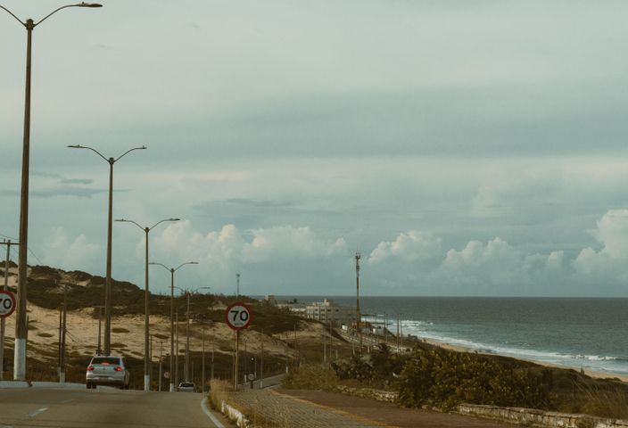Coastal road scene with sandy dunes and ocean view in Natal, Brazil at daytime.