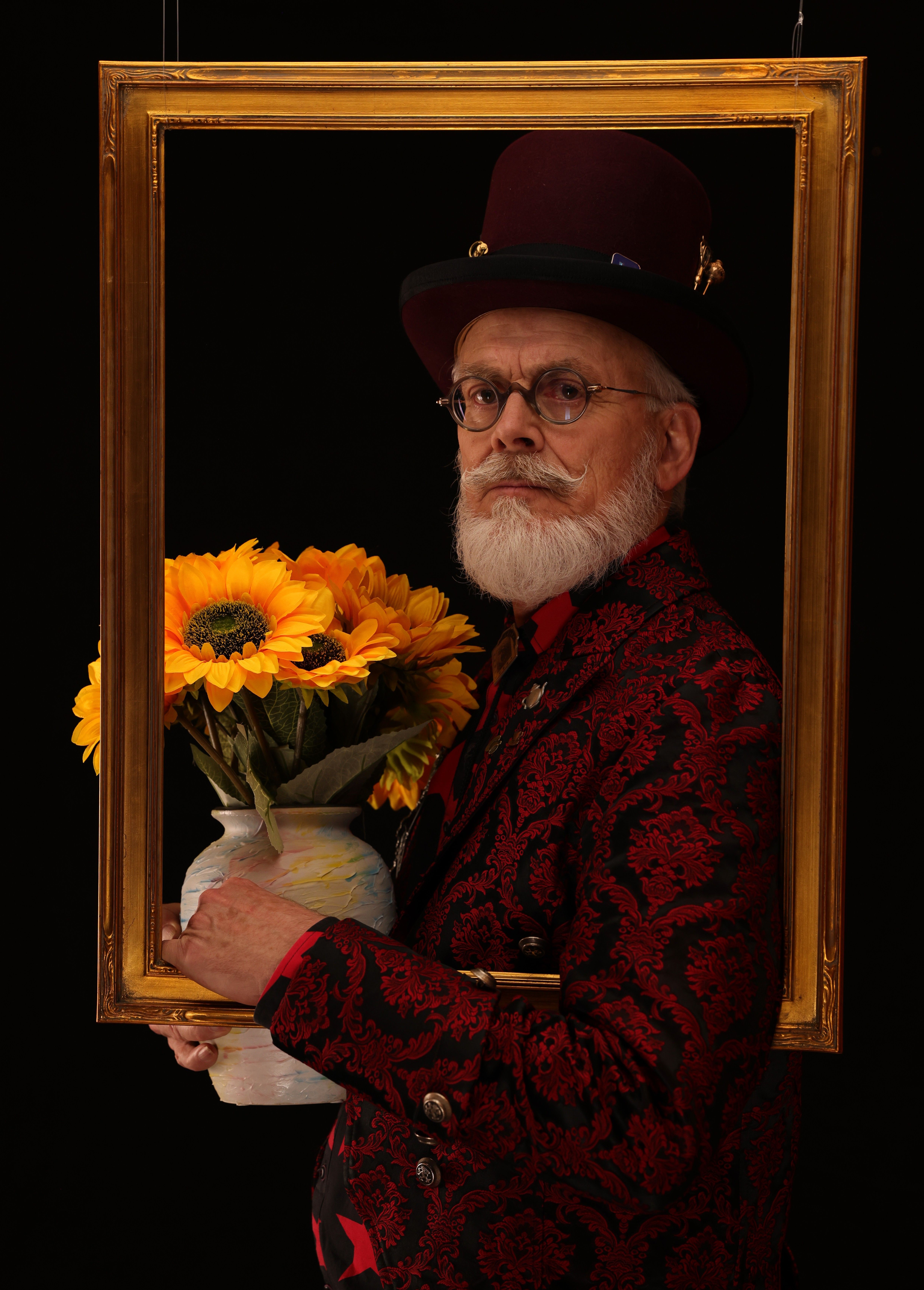 A man in vintage attire holds a sunflower vase in a frame, blending artistry and whimsy.