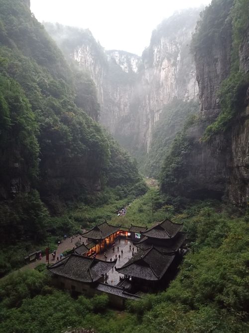 Free A dramatic view of a Chinese valley with traditional buildings nestled amid lush cliffs. Stock Photo