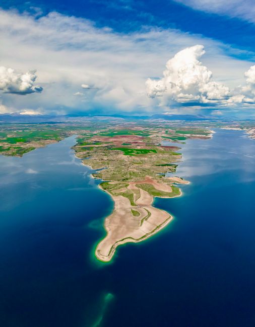 Breathtaking aerial view of the Euphrates River and lush landscape in Adıyaman, Türkiye, under a bright blue sky with clouds.