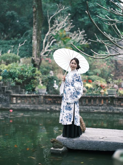 Elegant Vietnamese woman with parasol by a tranquil pond, showcasing traditional attire.