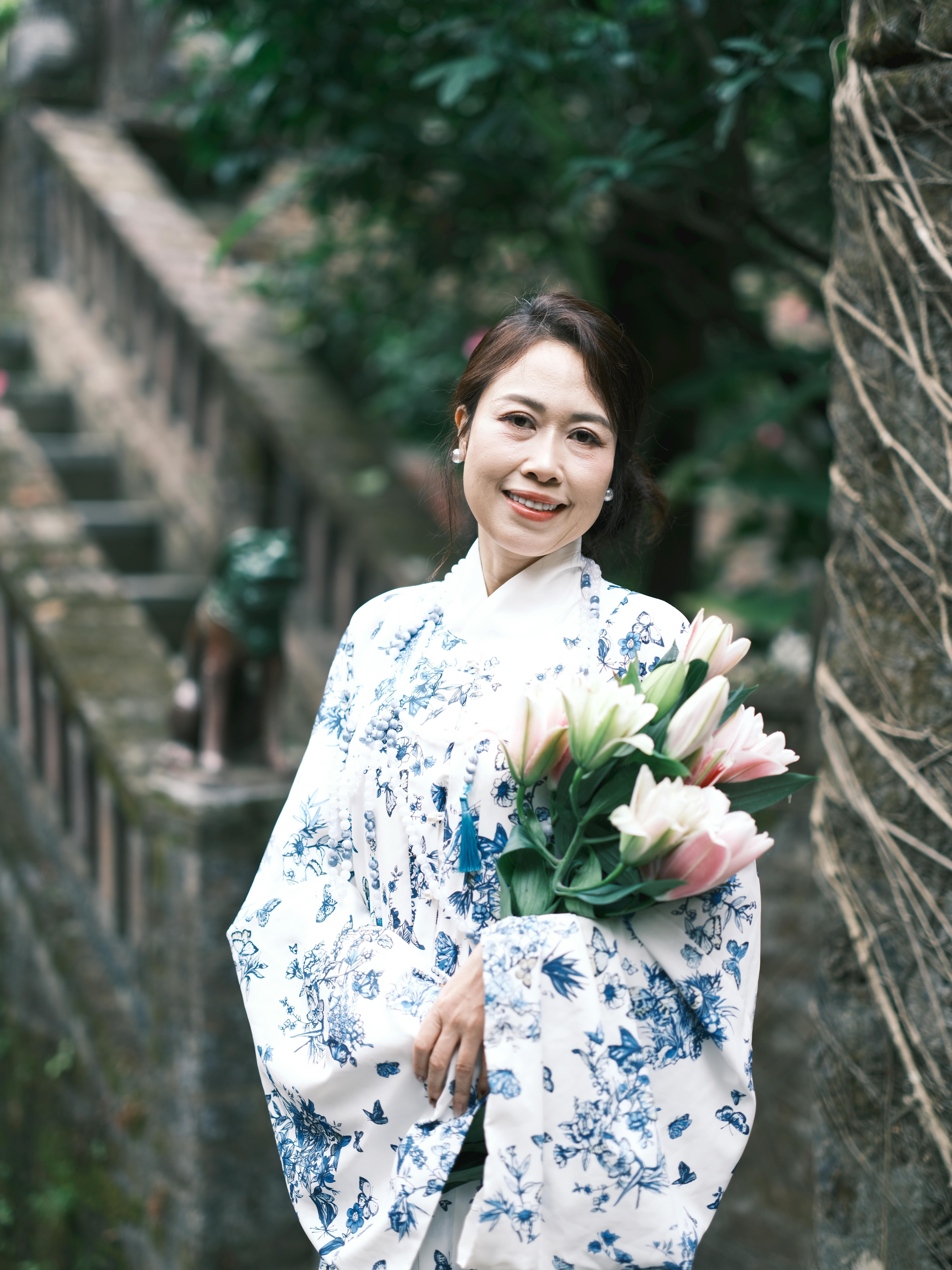 Elegant woman in a floral dress holding a bouquet of lilies in a serene Vietnamese garden.