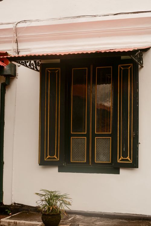 Free Decorative colonial-style window with dark green shutters and ornate detailing, capturing historic architecture charm. Stock Photo