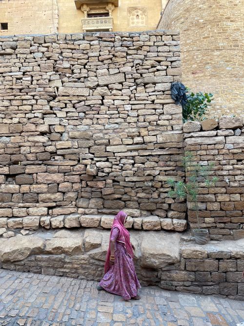 Free A woman in a pink sari strolls past an ancient stone wall in Jaisalmer, India. Stock Photo