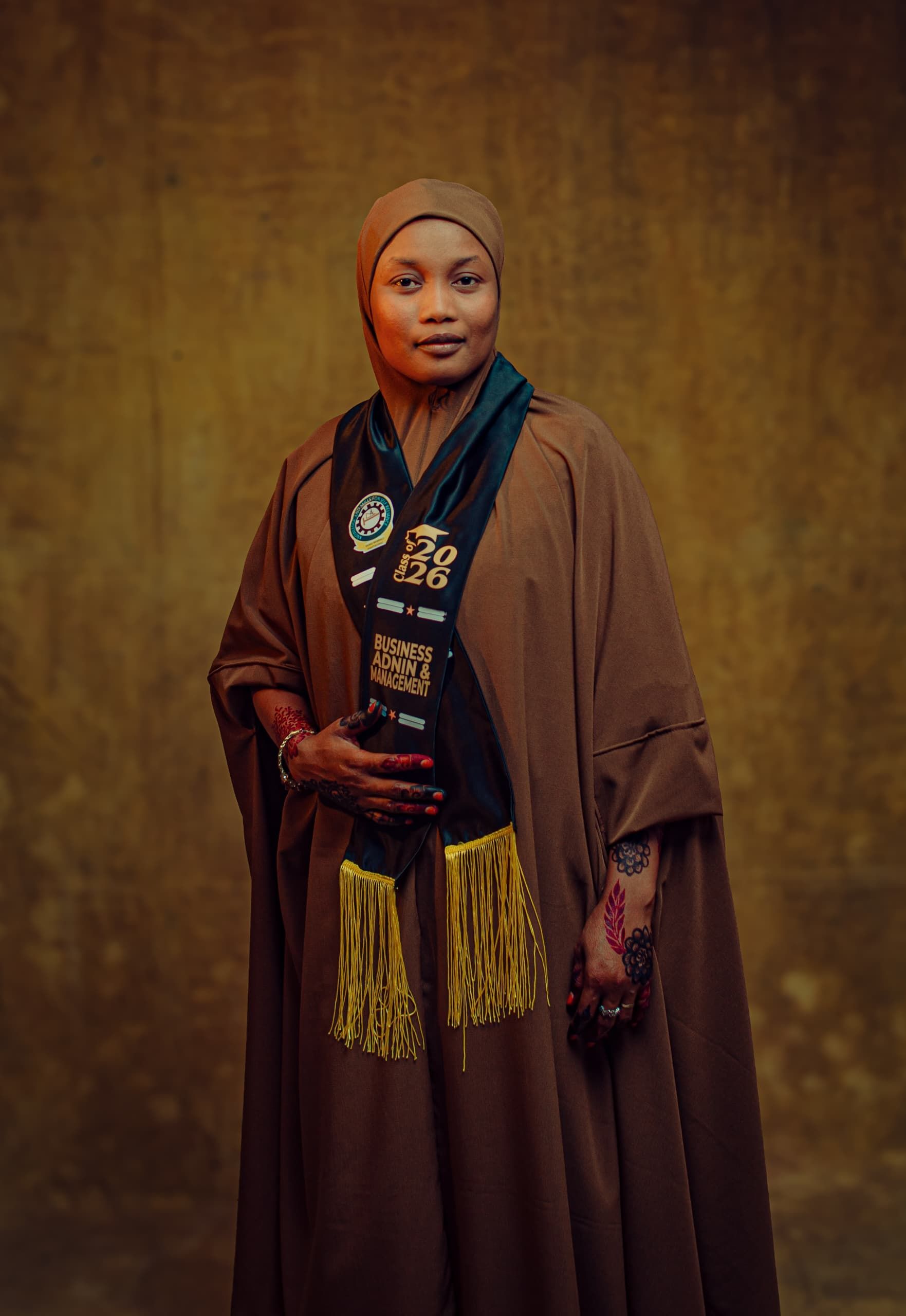 Confident woman in brown robe with headscarf celebrating graduation.