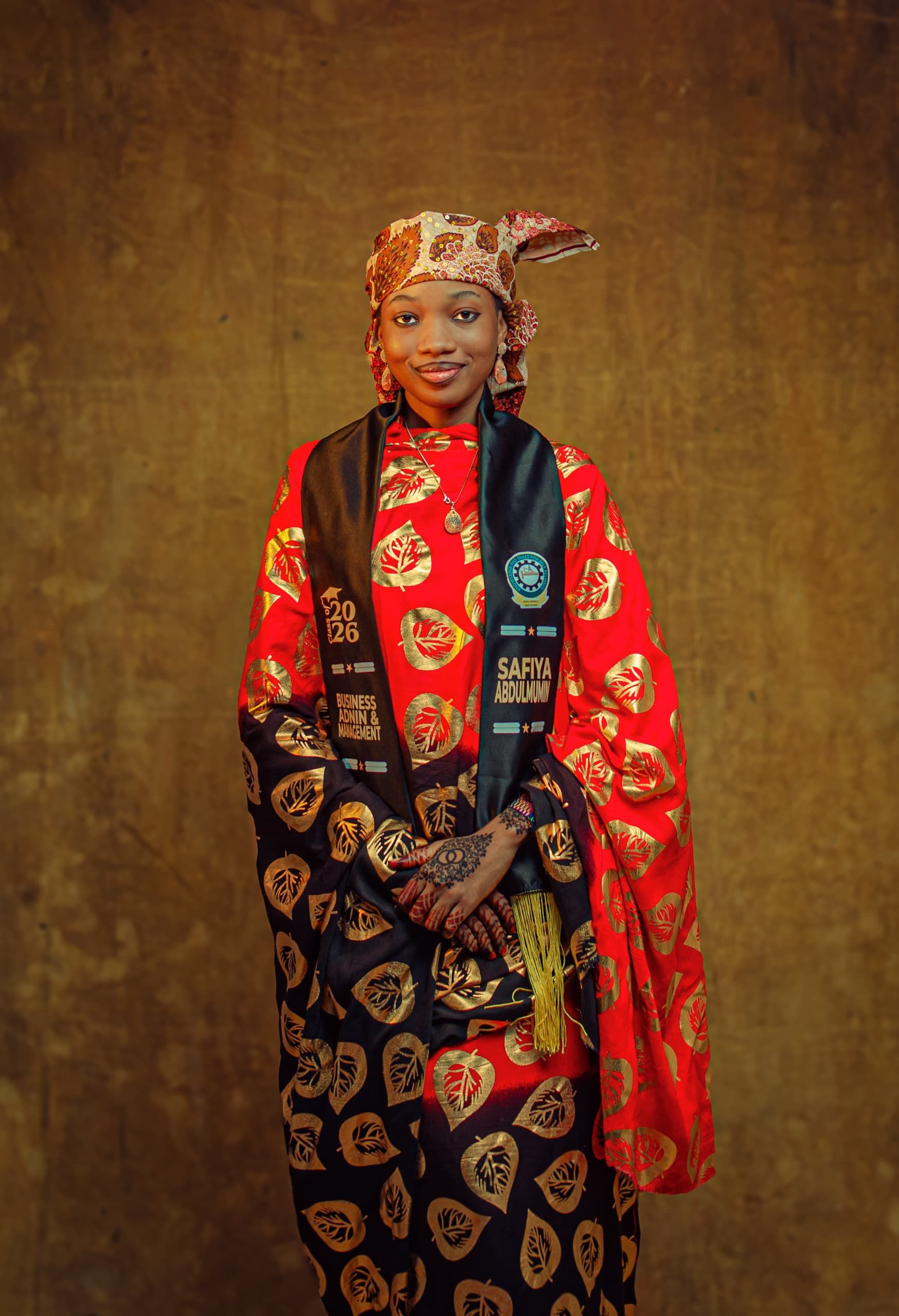 Woman in vibrant traditional dress and headscarf with a graduation sash.