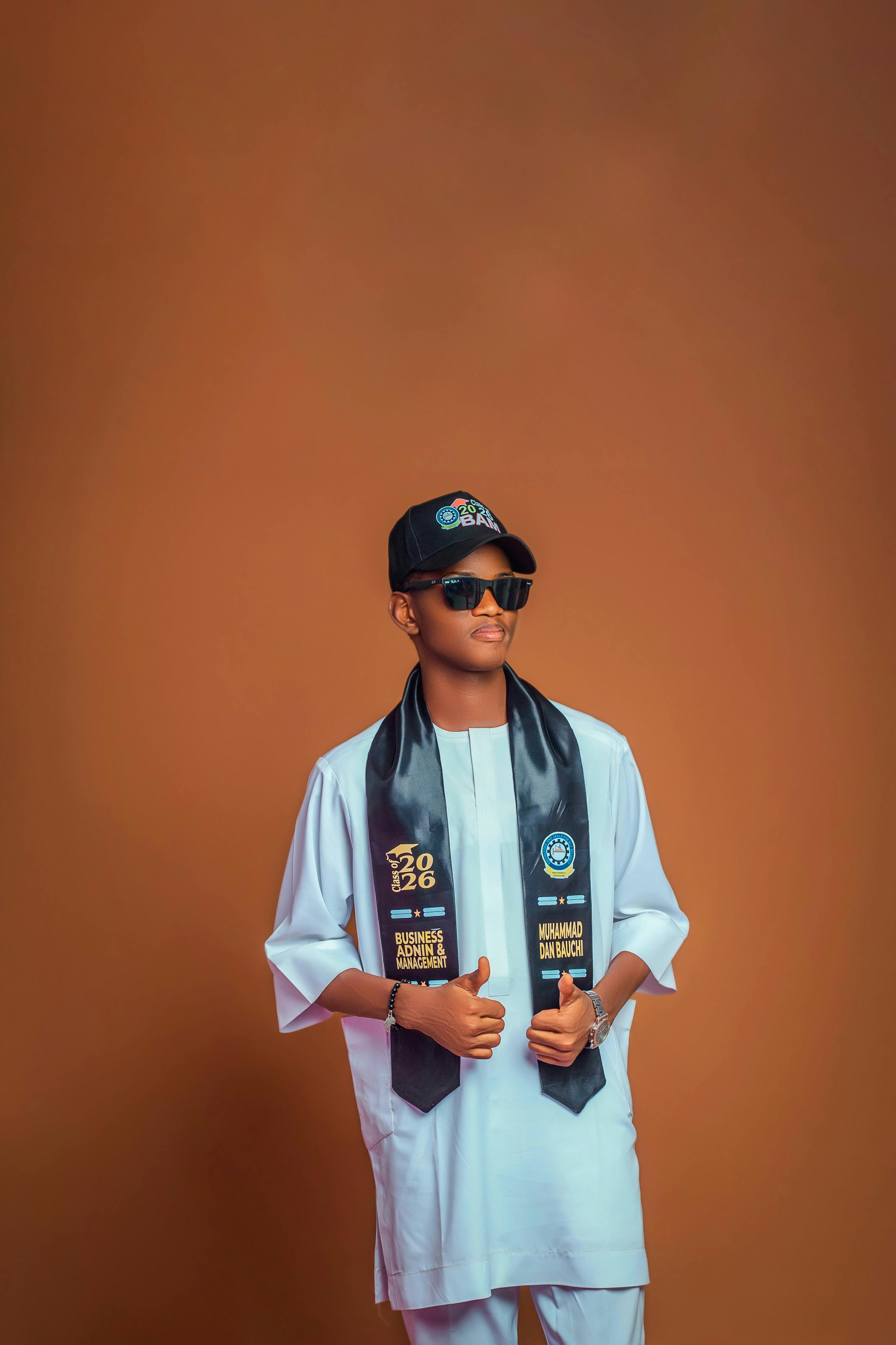 Confident young man in graduation attire giving thumbs up against solid background.