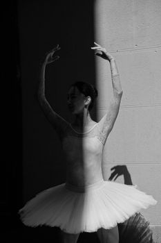 Black and white photo of a graceful ballerina in a tutu, captured in a dramatic shadow.