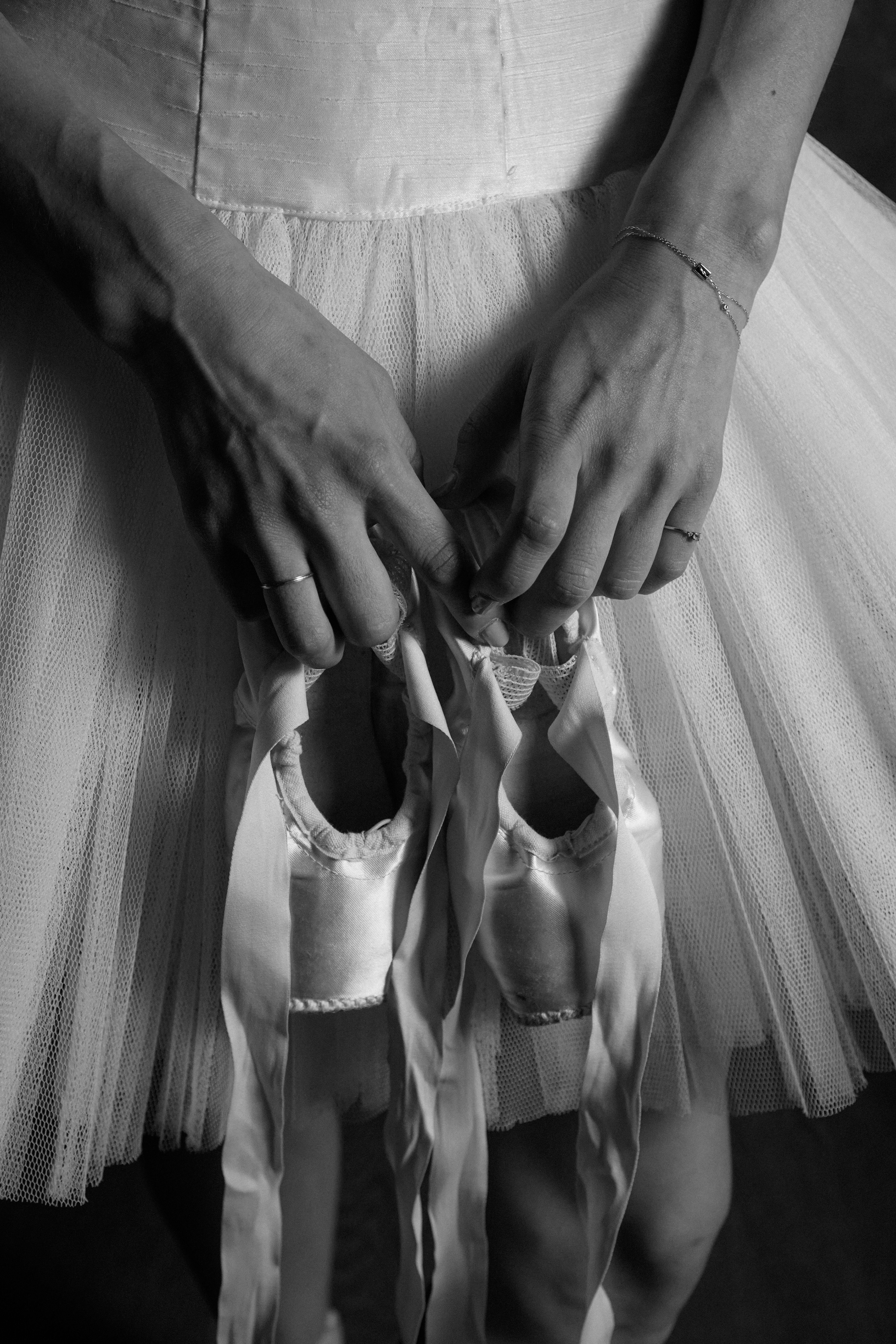 A ballerina in a tutu holding pointe shoes, captured in a moody black and white style.