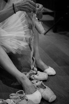 Black and white image of a ballerina tying her pointe shoes, captured indoors.