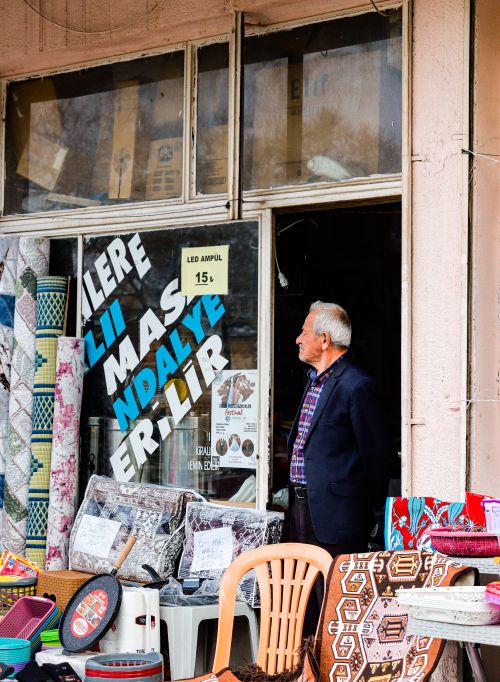Free Senior man stands at a shop entrance with an array of textiles on display. Stock Photo