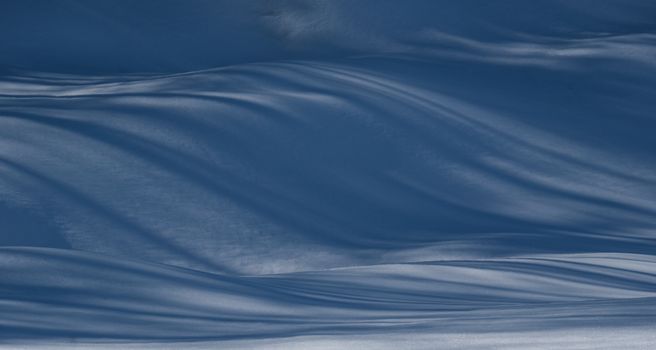 Artistic shadows cast over a snowy landscape create a serene abstract design, capturing the essence of winter.