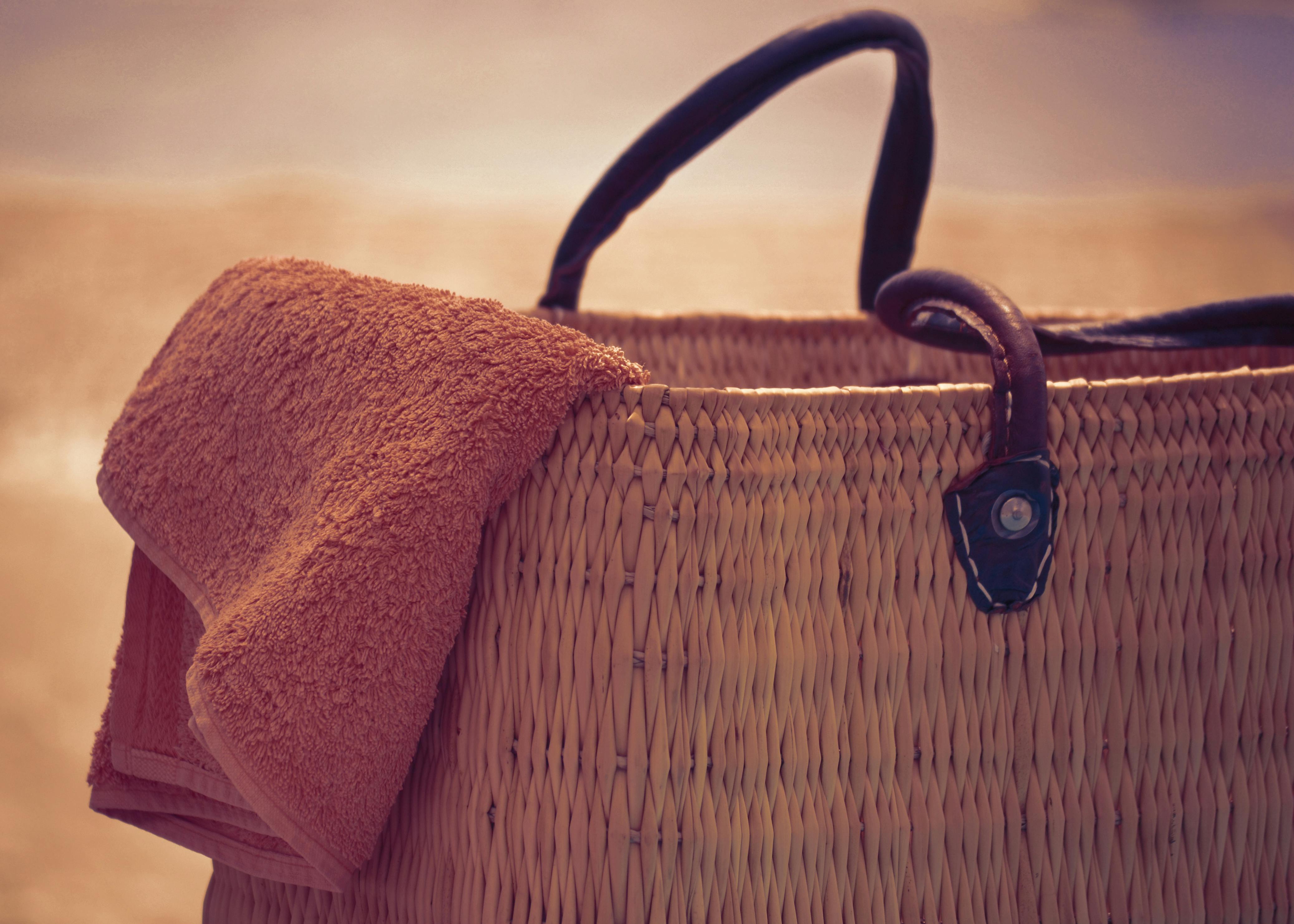 A straw beach bag with a towel draped over it, perfect for a summer day at the shore.