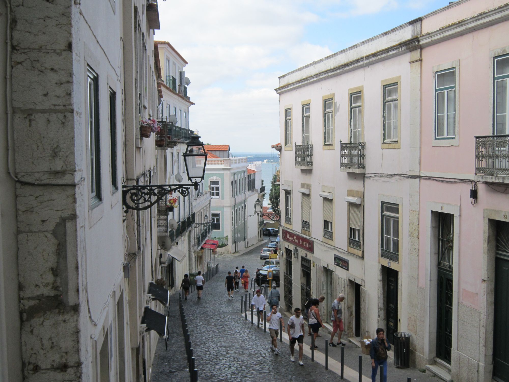 Discover the charm of a Lisbon alley with old buildings and a scenic view towards the sea.