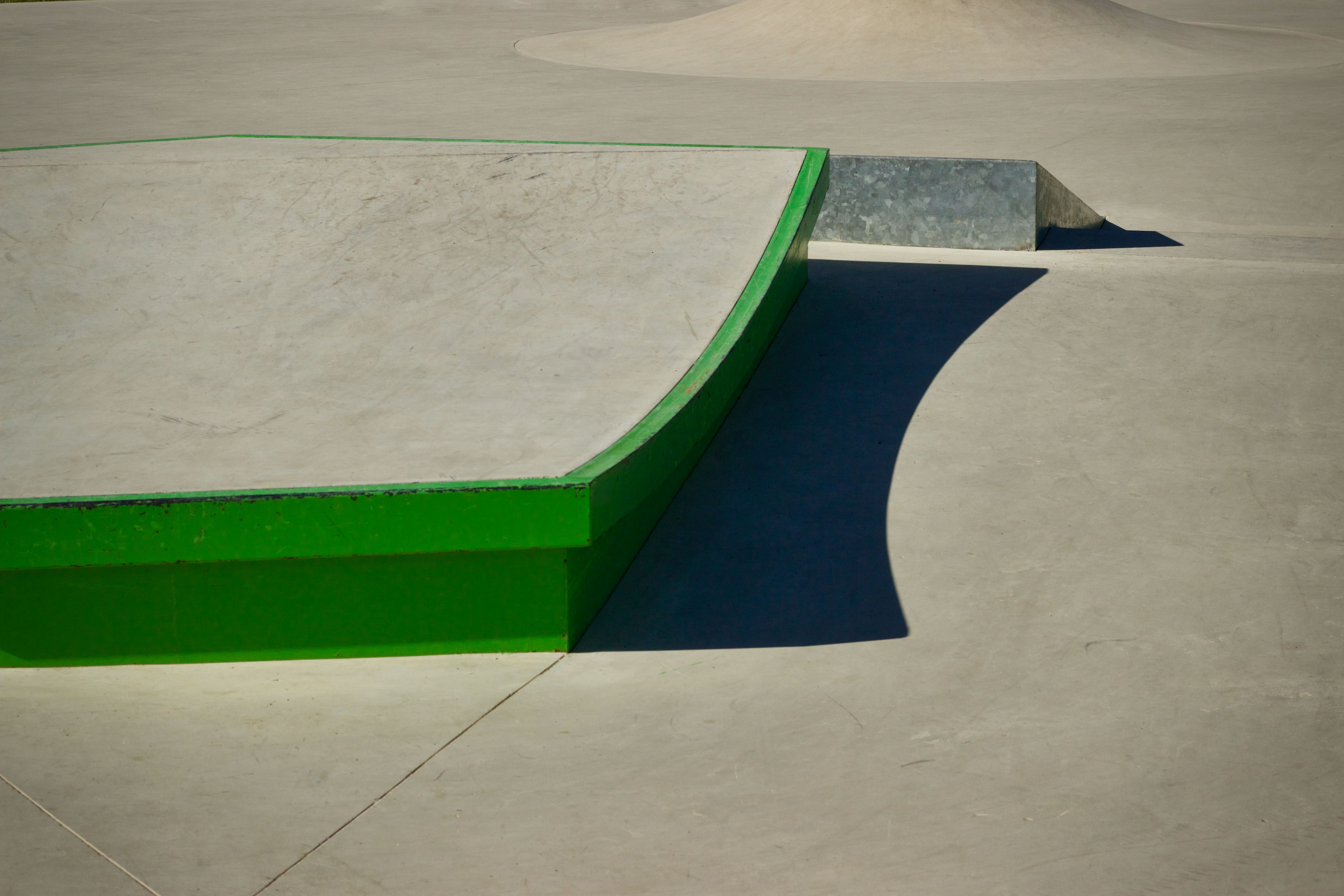 Long dramatic shadows stretching across smooth curved concrete skatepark ramps