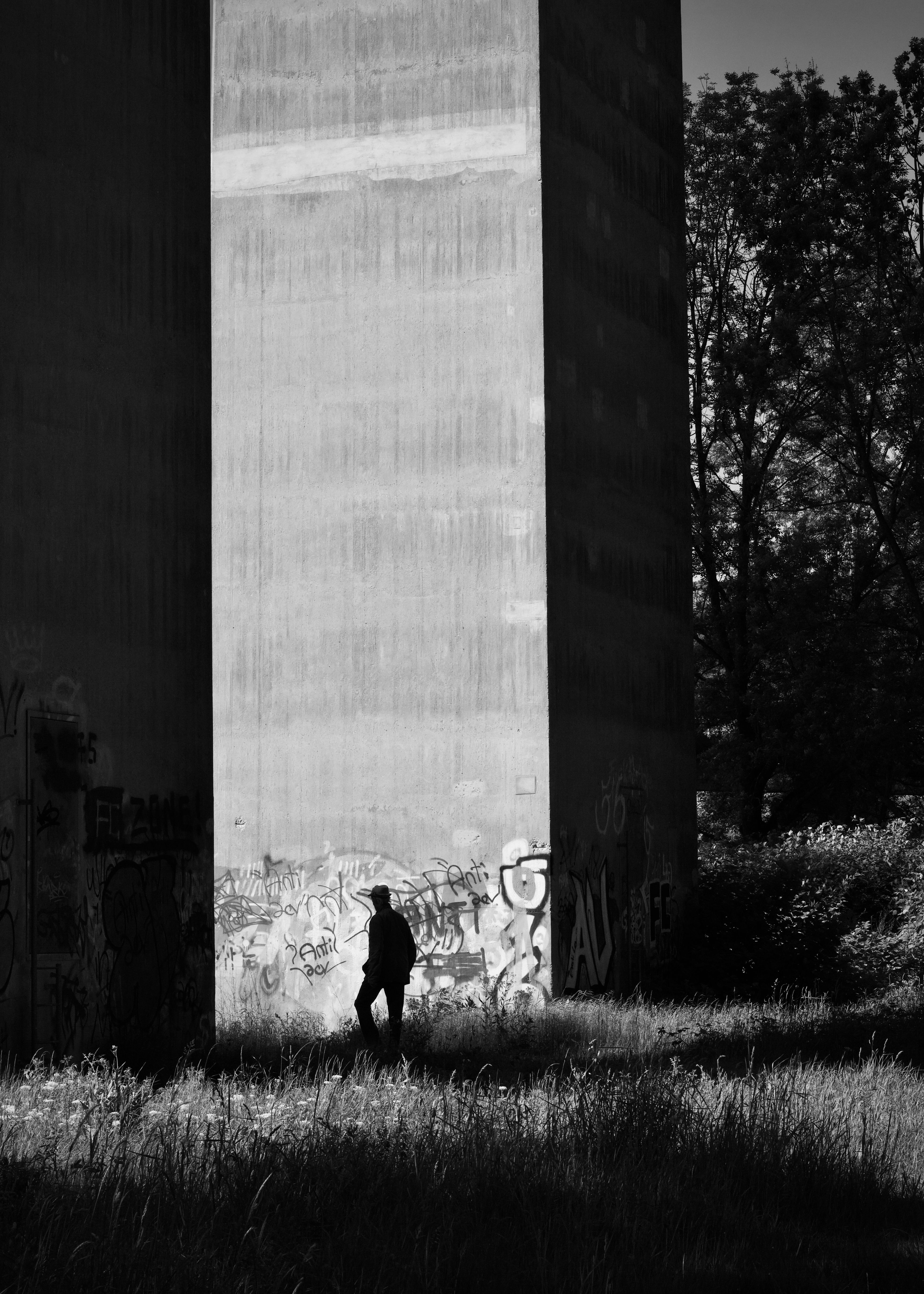A person walks past a graffiti-covered wall in a shadowy urban scene, emphasizing solitude.