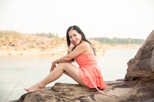 Positive Asian woman resting on rocky coastline